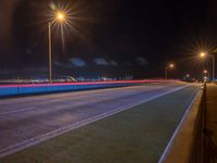 a road with multiple lights near the road and a sky line in the background and cars passing by