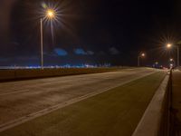 a road with multiple lights near the road and a sky line in the background and cars passing by