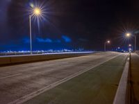 a road with multiple lights near the road and a sky line in the background and cars passing by