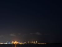 an airplane flies over the city on the ocean at night, with bright light and clouds