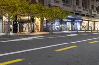 a sidewalk and a street corner at night time with trees growing on each side of it