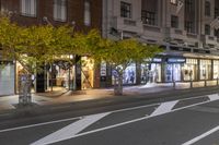 a sidewalk and a street corner at night time with trees growing on each side of it