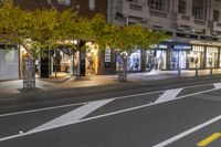 a sidewalk and a street corner at night time with trees growing on each side of it