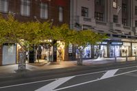 a sidewalk and a street corner at night time with trees growing on each side of it