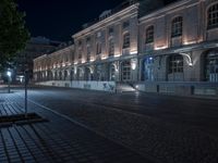 a night time image of a man on a bicycle on the street in front of a building