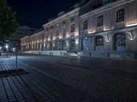 a night time image of a man on a bicycle on the street in front of a building