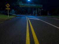 the street lights are shining at night under the bridge over the road, with a yellow line on the road next to the fence