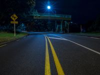 the street lights are shining at night under the bridge over the road, with a yellow line on the road next to the fence