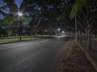 a empty street at night with many trees around it and lights shining in the background