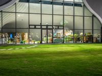 a large white building with a big glass door and several plants inside of it at night