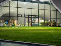 a large white building with a big glass door and several plants inside of it at night