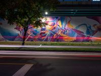 a person walking in front of a painted wall on the side of the road at night