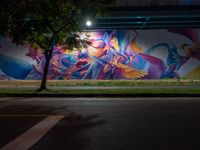 a person walking in front of a painted wall on the side of the road at night