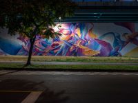 a person walking in front of a painted wall on the side of the road at night