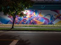 a person walking in front of a painted wall on the side of the road at night