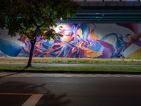 a person walking in front of a painted wall on the side of the road at night