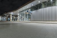 a paved area at night, with a tall building and white facade lit up by low - fi light