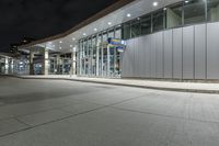 a paved area at night, with a tall building and white facade lit up by low - fi light