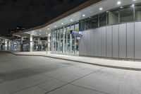 a paved area at night, with a tall building and white facade lit up by low - fi light