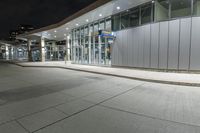 a paved area at night, with a tall building and white facade lit up by low - fi light