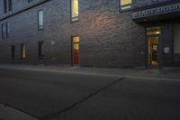 an empty sidewalk in front of a brick building and two story doors on either side of the building