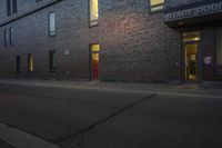 an empty sidewalk in front of a brick building and two story doors on either side of the building