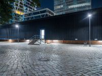 night scene in public parking area with lights on and steps up to building behind it