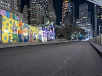 an empty roadway at night with lights shining on buildings in the background and a colorful mural