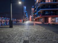 the sidewalk has several bricks on it at night near many tall buildings and a clock tower