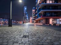 the sidewalk has several bricks on it at night near many tall buildings and a clock tower