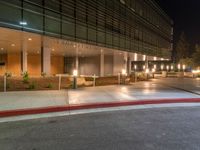 a street corner with a sidewalk and some lights on at night time with a black sky background