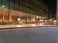 a street corner with a sidewalk and some lights on at night time with a black sky background