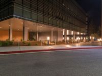 a street corner with a sidewalk and some lights on at night time with a black sky background