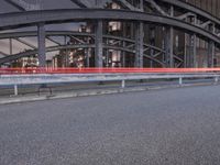 a car passing a bridge that is next to another building in the background with street lights in front of it