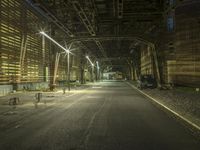 an empty long street with a car at the end of it at night time near a large factory