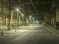 an empty long street with a car at the end of it at night time near a large factory