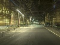 an empty long street with a car at the end of it at night time near a large factory