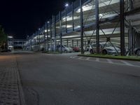 some cars are parked inside the parking lot at night time and there is a walkway to the left