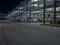 some cars are parked inside the parking lot at night time and there is a walkway to the left