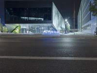 an empty street in front of a glass building at night with the words mutipin lit in bright blue on it