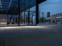 a parking area and sidewalk at night with several benches underneath the roof with windows lit up