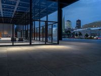 a parking area and sidewalk at night with several benches underneath the roof with windows lit up