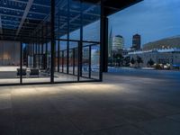 a parking area and sidewalk at night with several benches underneath the roof with windows lit up