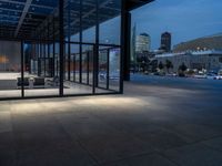 a parking area and sidewalk at night with several benches underneath the roof with windows lit up