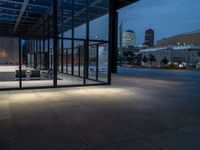 a parking area and sidewalk at night with several benches underneath the roof with windows lit up