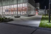 the empty courtyard at night outside an office building with glass walls and lots of lights