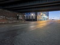 an urban road at night with no cars in sight of the light coming through a bridge