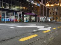 a city street at night with the lights on in a building behind it and on the ground at the intersection