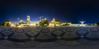 a circular photograph of city buildings with benches in the center at night time and blue sky