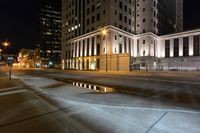 some buildings a street and some cars on the road at night time? in the city
